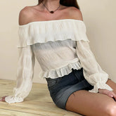 Woman wearing an off-shoulder ruffled top and denim shorts on a wooden floor.